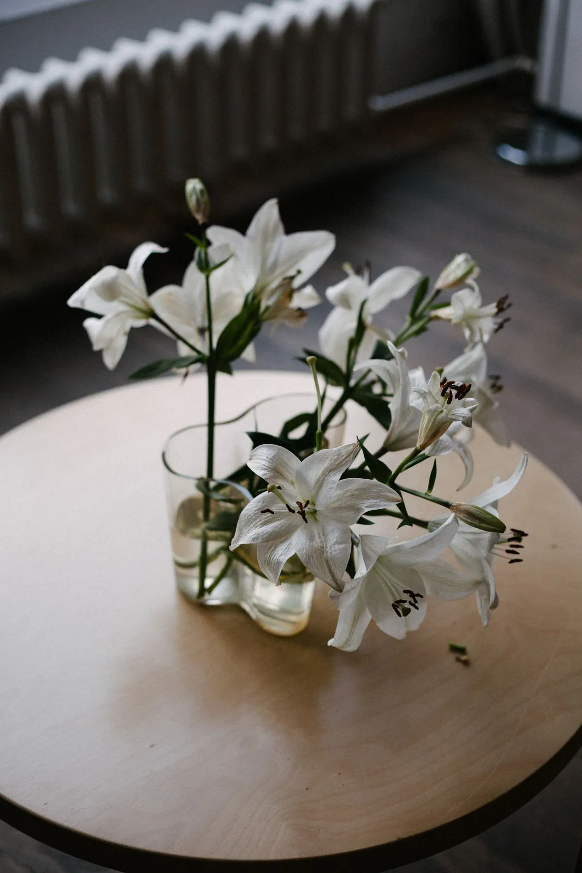 White lilies arranged in a glass vase on a wooden table