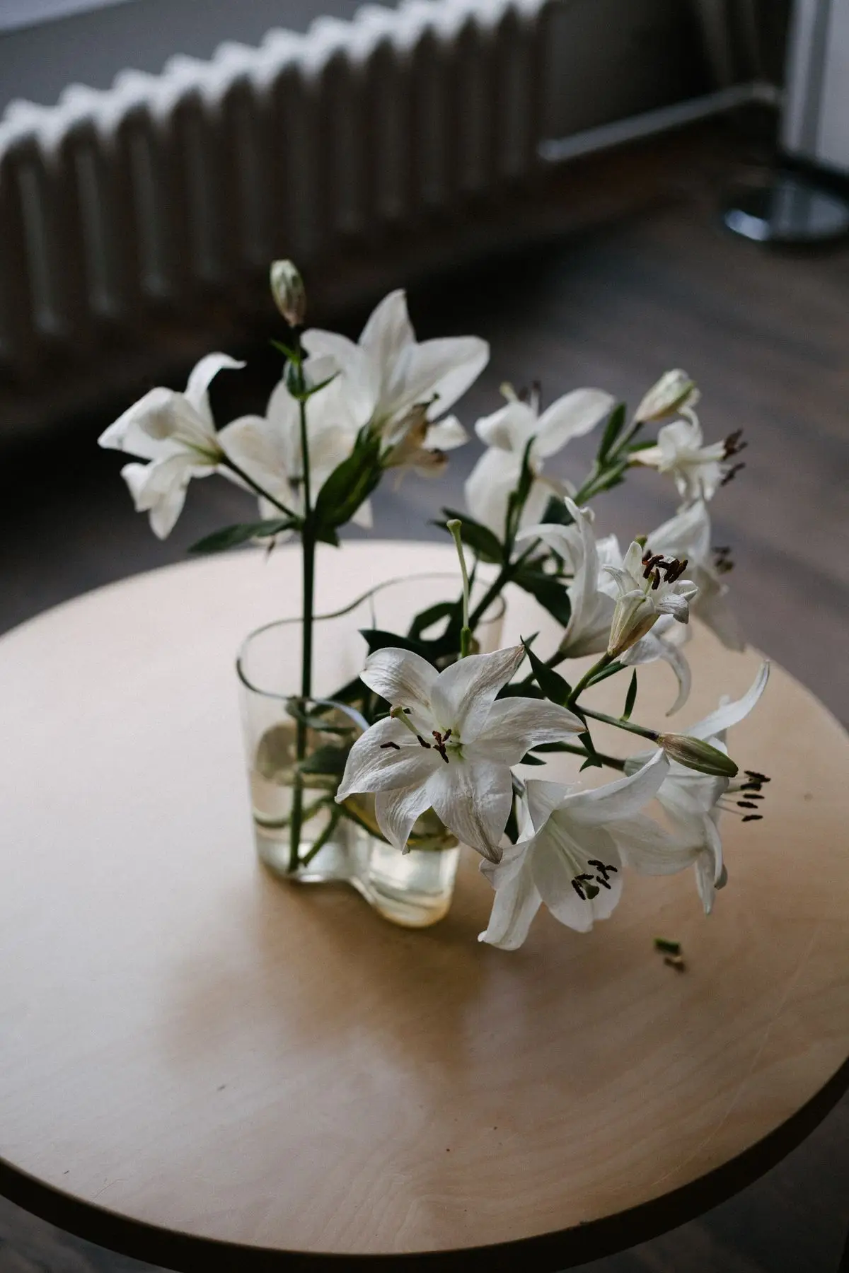 White lilies arranged in a glass vase on a wooden table